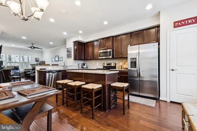 a kitchen with stainless steel appliances kitchen island granite countertop a refrigerator a stove a sink a dining table and chairs with wooden floor