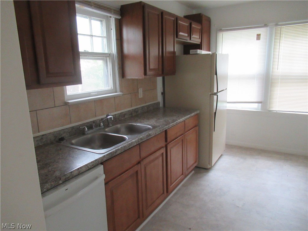 3824 East Antisdale Road Cleveland, OH 44118 - Photo 10 of 27 Kitchen featuring wood-finish cabinetry, a double basin stainless steel sink, tile backsplash, and two windows with horizontal blinds