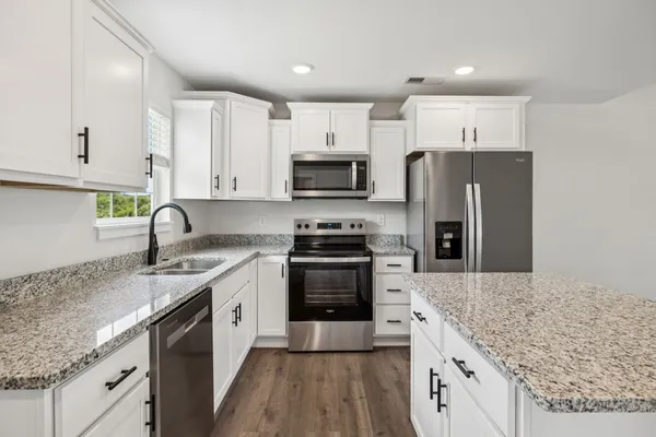 a kitchen with stainless steel appliances granite countertop a refrigerator a stove a sink and white cabinets