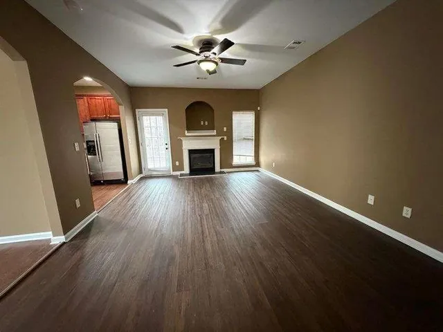 a view of an empty room with wooden floor a ceiling fan and windows