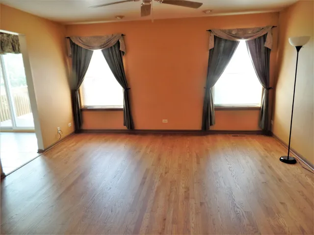 a view of empty room with wooden floor and fan