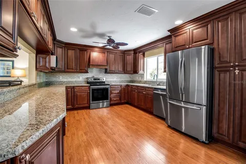 a kitchen with stainless steel appliances granite countertop a refrigerator oven a sink dishwasher and wooden cabinets with wooden floor