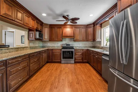 a kitchen with stainless steel appliances granite countertop a refrigerator a sink dishwasher a stove and a oven with wooden floor