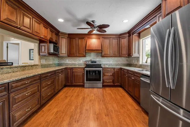 a kitchen with stainless steel appliances granite countertop a refrigerator a sink dishwasher a stove and a oven with wooden floor