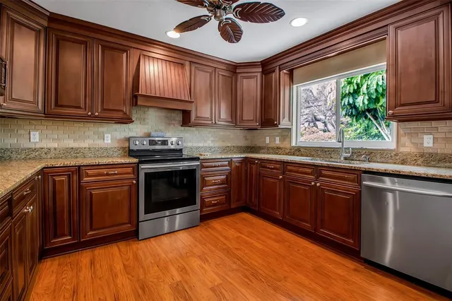 a kitchen with stainless steel appliances granite countertop wooden cabinets a stove a sink and dishwasher with wooden floor