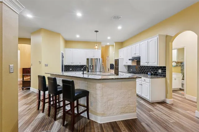 a kitchen with stainless steel appliances kitchen island granite countertop a table chairs sink and cabinets