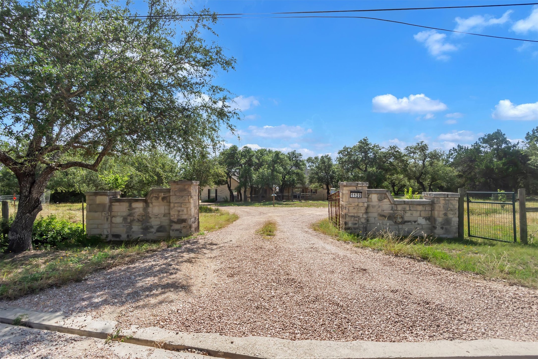 1120 Meadow Ridge Drive Austin, TX 78737 - Photo 2 of 40 A private gravel driveway leads through sturdy stone pillars to a secluded residence surrounded by mature trees.