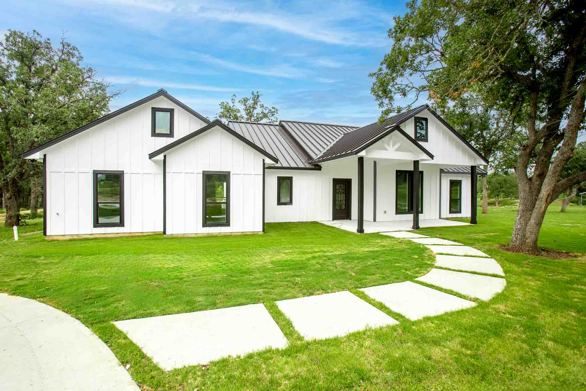 337 Smitty Lane Lockhart, TX 78644 - Photo 1 of 40 A modern farmhouse design with striking black trim and a metal roof, framed by verdant landscaping.