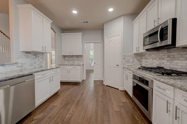 a kitchen with stainless steel appliances white cabinets a sink a stove a microwave and wooden floors