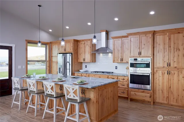 a kitchen with stainless steel appliances granite countertop a stove top oven a sink dishwasher and white cabinets with wooden floor