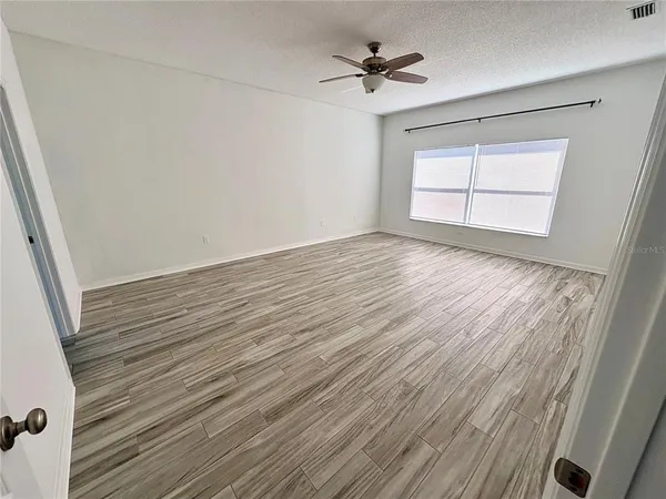 a view of empty room with wooden floor and fan