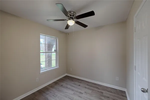 an empty room with wooden floor ceiling fan and windows
