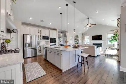 a kitchen with stainless steel appliances kitchen island a refrigerator a stove a oven a sink dishwasher and white cabinets with wooden floor