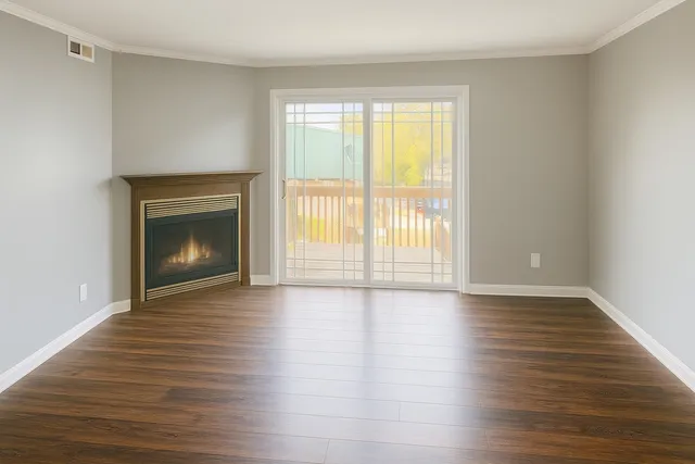a view of an empty room with wooden floor fireplace and a window