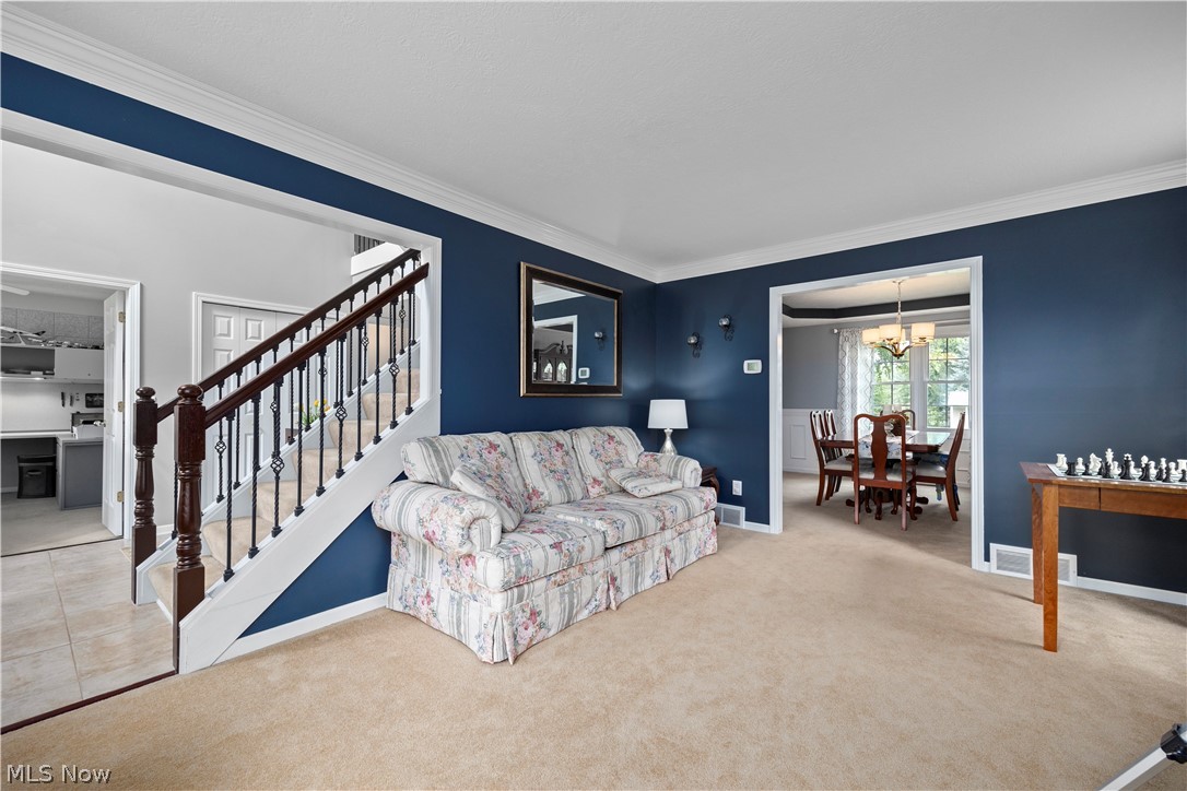 Staircase with dark wood handrail and decorative metal balusters, crown molding, cased openings, and neutral carpet flooring