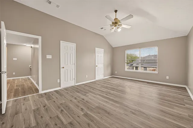 a view of an empty room with wooden floor and a chandelier fan