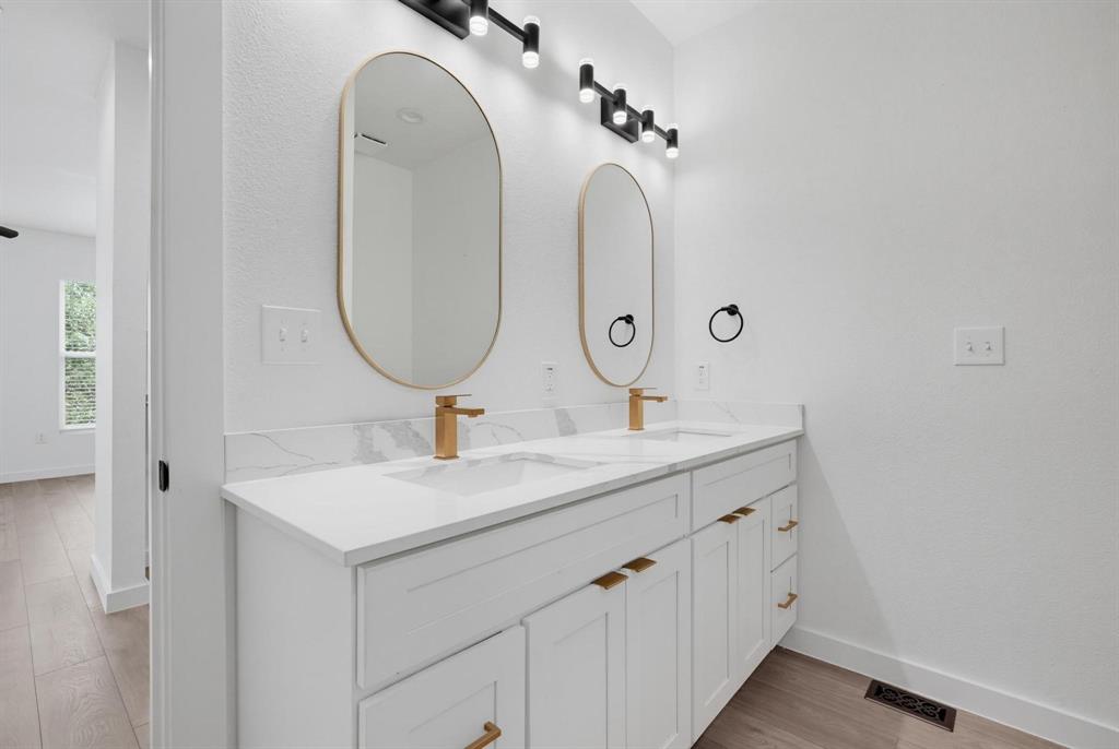 510 South O Connor Road Irving, TX 75060 - Photo 14 of 22 Double vanity featuring white cabinetry with gold-finish hardware, individual oval mirrors with gold-finish frames, and a white countertop with a subtle marble-look backsplash