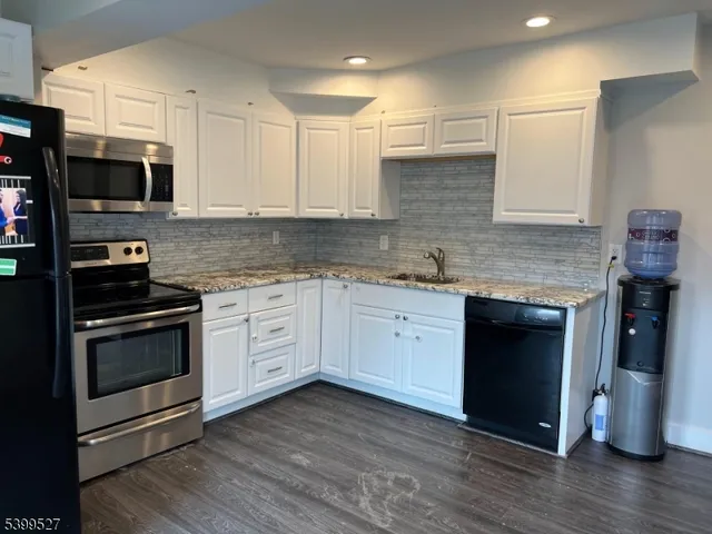 a kitchen with stainless steel appliances white cabinets a sink and wooden floor
