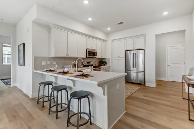 a kitchen with stainless steel appliances granite countertop a refrigerator a stove a sink a dining table and chairs with wooden floor