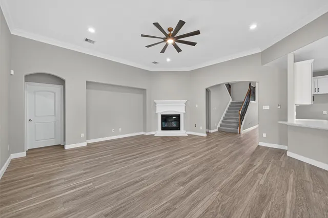 a view of an empty room with wooden floor and a ceiling fan