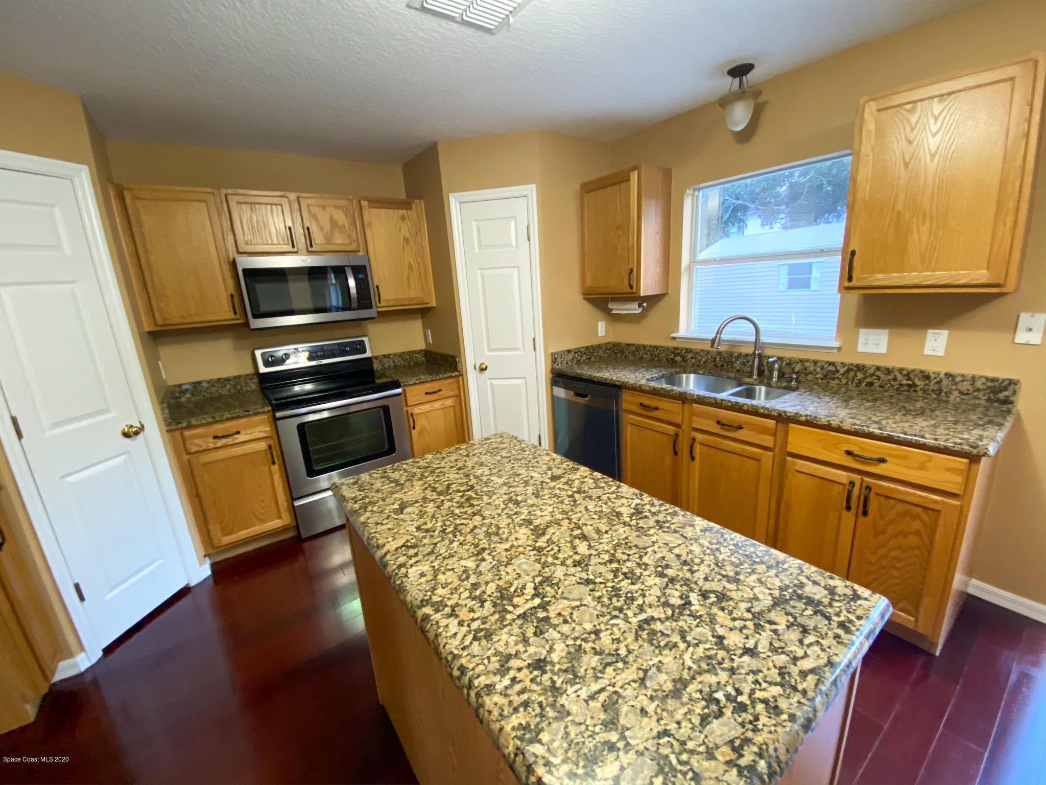 6150 Degan Road Cocoa, FL 32927 - Photo 14 of 48 a kitchen with stainless steel appliances kitchen island granite countertop a sink stove microwave and wooden floor