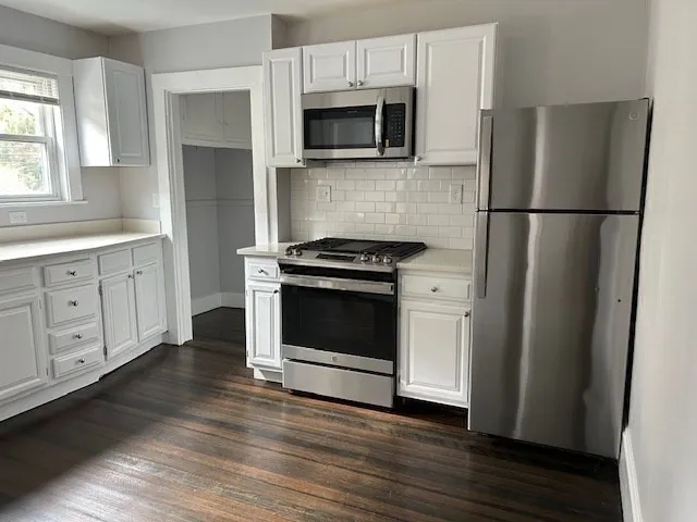 a kitchen with white cabinets stainless steel appliances and wooden floor