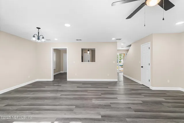 a view of an empty room with wooden floor and a ceiling fan