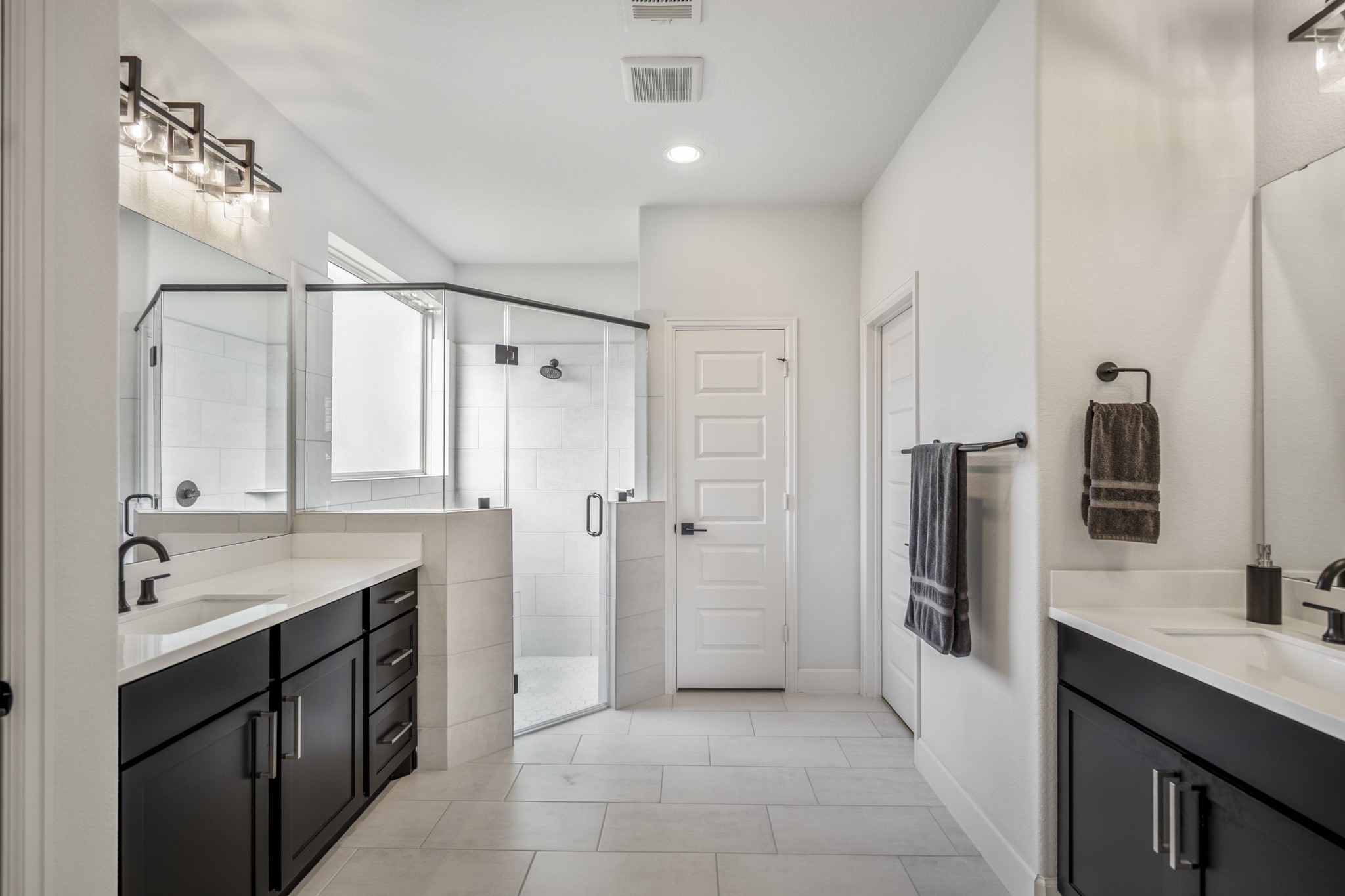 304 Mullins Court Montgomery, TX 77316 - Photo 15 of 50 This modern primary bathroom features dual vanities with sleek black cabinets, a spacious glass-enclosed shower, and elegant lighting fixtures, all set against crisp white walls and tile flooring.