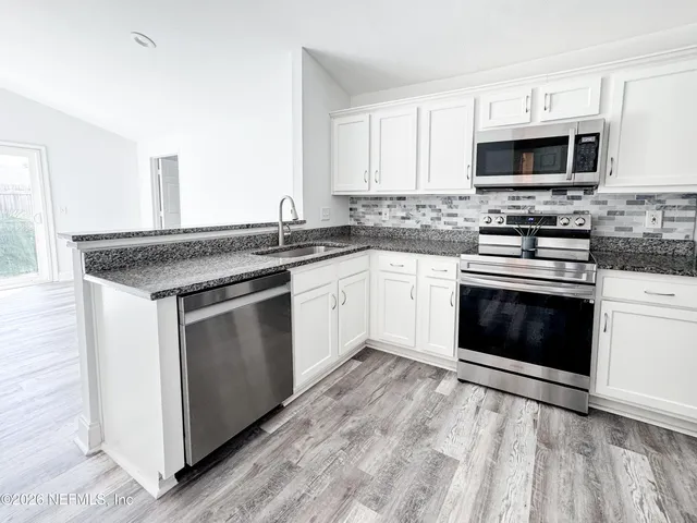 a white kitchen with granite countertop a stove top oven microwave and cabinets