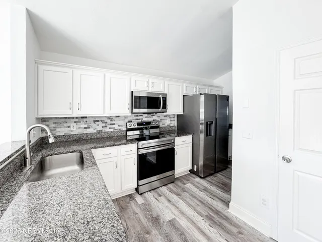 a kitchen with granite countertop a stove a sink and a refrigerator