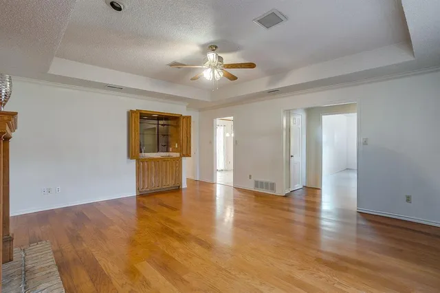 an empty room with wooden floor chandelier fan and windows