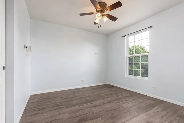 an empty room with wooden floor fan and windows