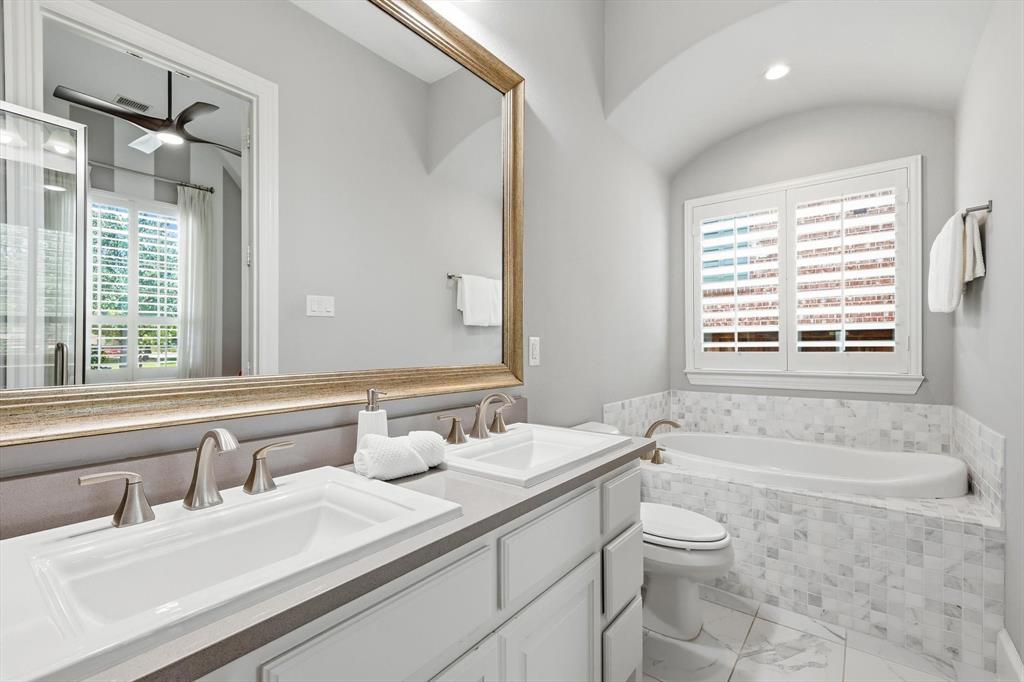 1933 Snapdragon Road Frisco, TX 75033 - Photo 25 of 40 Bathroom featuring a dual vanity with undermount sinks, brushed nickel fixtures, a built-in bathtub with mosaic tile surround, and plantation shutters