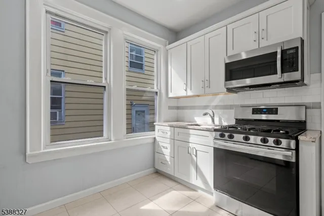 a kitchen with stainless steel appliances granite countertop grey cabinets a stove a microwave and a window