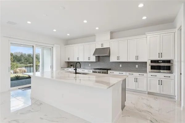a large kitchen with stainless steel appliances granite countertop a stove a sink a refrigerator and white cabinets