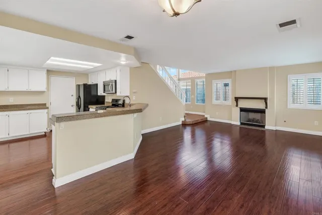 a view of a kitchen and an empty room with wooden floor and a kitchen