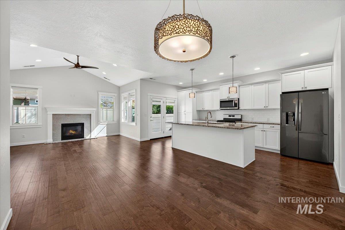 4204 East Silverking Lane Meridian, ID 83642 - Photo 11 of 40 Open-concept living space featuring wood-finish flooring, a white kitchen island with pendant lighting, and an integrated fireplace with a mantel