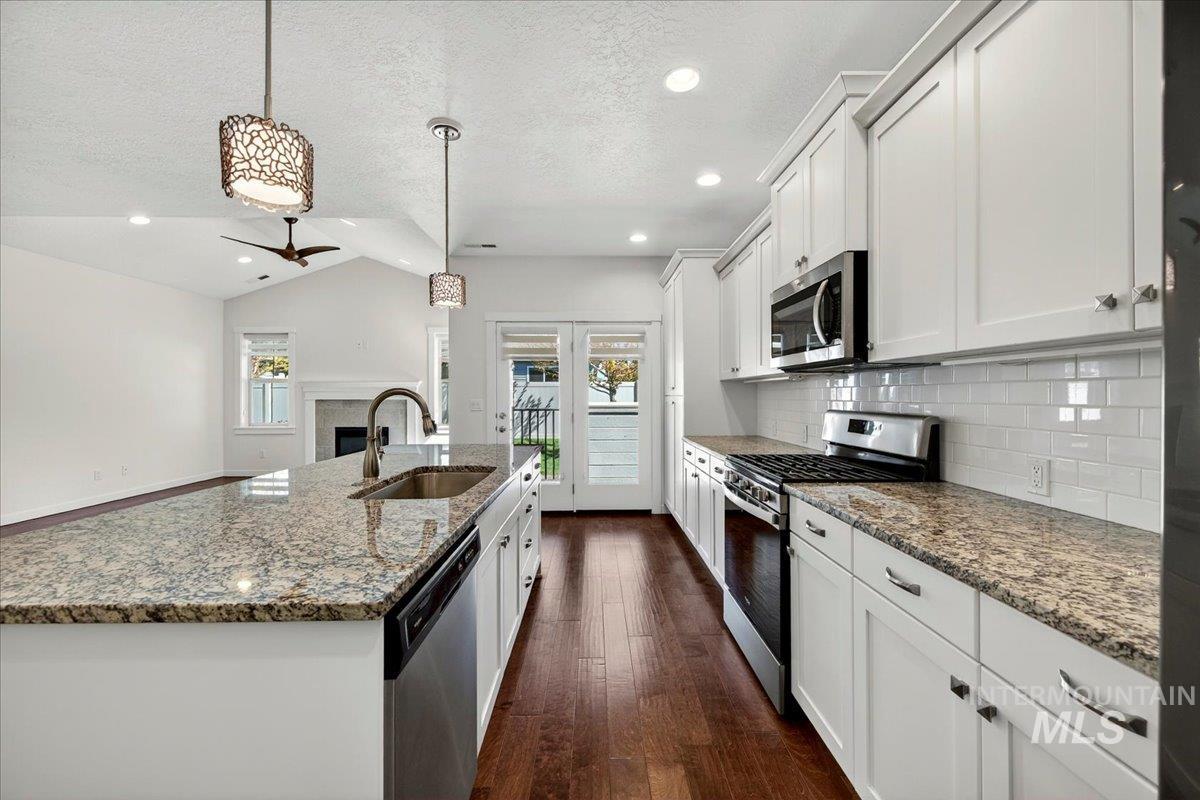 4204 East Silverking Lane Meridian, ID 83642 - Photo 16 of 40 Open-concept kitchen featuring an oversized island with an undermount sink, granite countertops, white cabinetry, stainless steel appliances, and wood-finish flooring