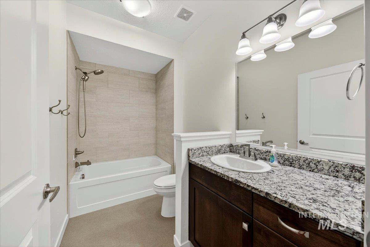 4204 East Silverking Lane Meridian, ID 83642 - Photo 19 of 40 Bathroom vanity featuring a granite countertop with an undermount sink, dark wood cabinetry, and a large wall-mounted mirror