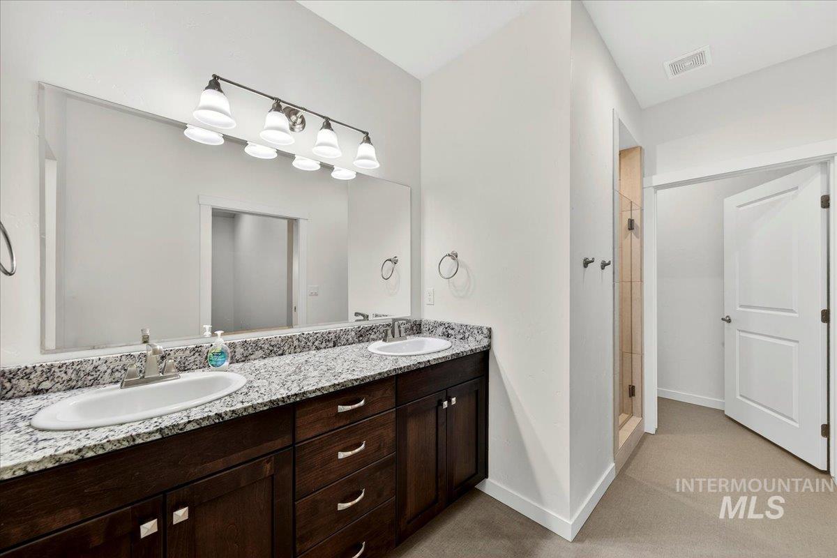 4204 East Silverking Lane Meridian, ID 83642 - Photo 26 of 40 Dual vanity with a stone-finish countertop, undermount sinks, and dark wood-finish cabinetry