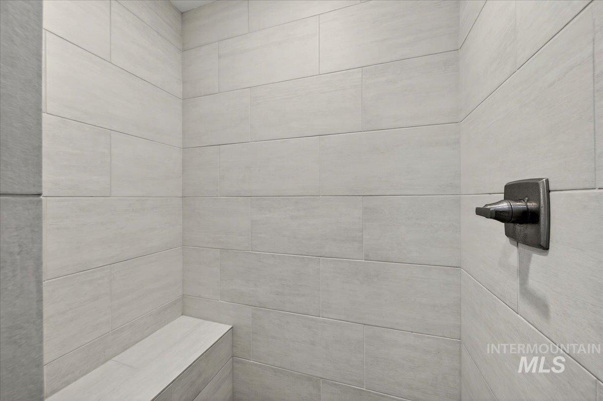 4204 East Silverking Lane Meridian, ID 83642 - Photo 27 of 40 Tiled shower with a built-in bench, neutral-toned rectangular wall tiles, and a dark bronze shower control handle