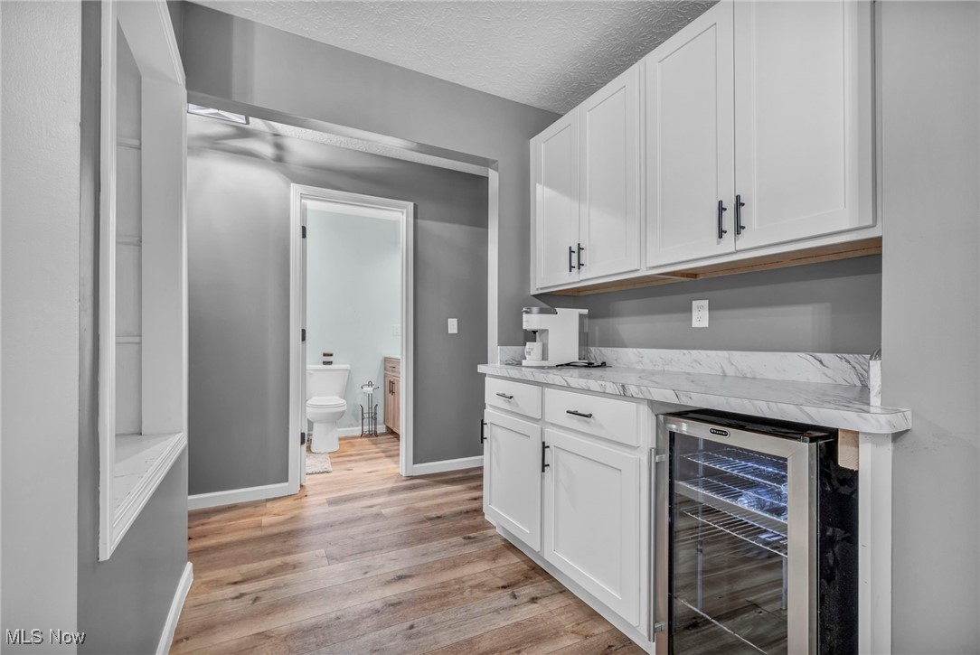 5306 Lockwood Road Madison, OH 44057 - Photo 13 of 28 Bar featuring white cabinets, light wood-type flooring, light stone counters, wine cooler, and a textured ceiling
