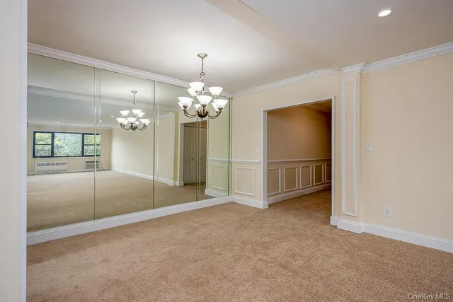 an empty room with chandelier fan and kitchen view