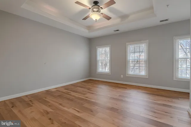 an empty room with wooden floor fan and windows