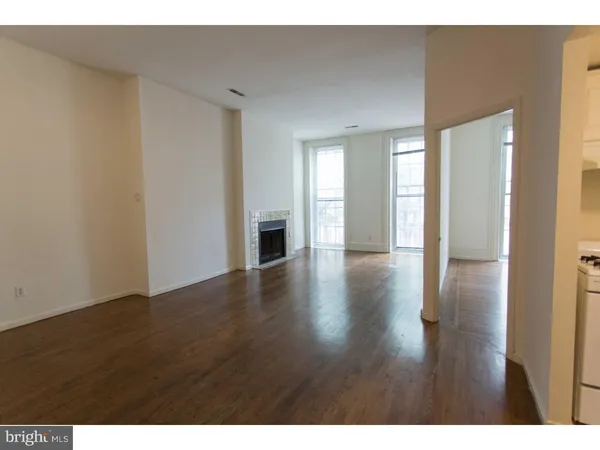 a view of an empty room with wooden floor and a fireplace