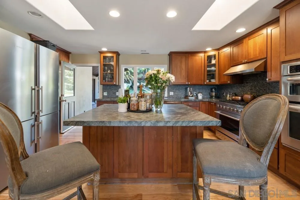 16919 Reposa Alta Rancho Santa Fe, CA 92067 - Photo 17 of 51 a kitchen with stainless steel appliances granite countertop a table chairs in it and wooden floors