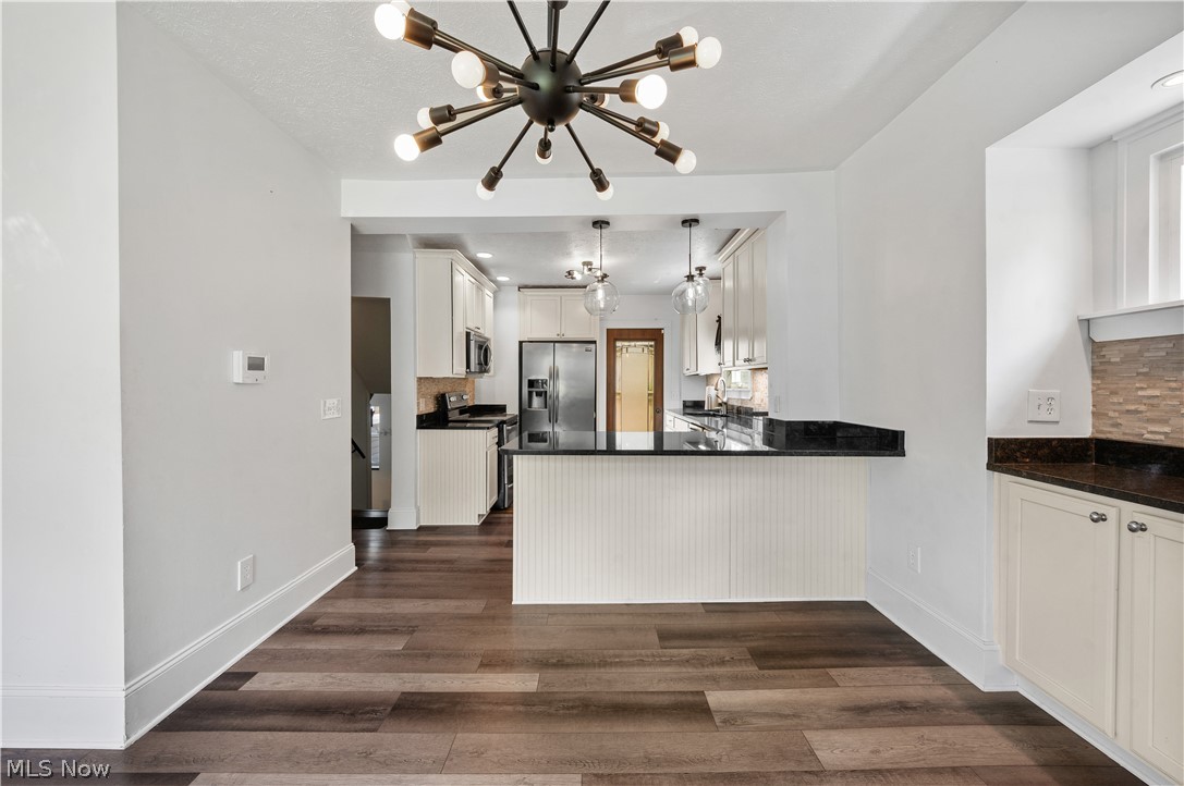 371 Merriman Road Akron, OH 44303 - Photo 8 of 27 Modern Sputnik-style chandelier with a dark bronze finish, wood-finish flooring, white baseboards, and a kitchen pass-through with a breakfast bar featuring black countertops and white beadboard paneling