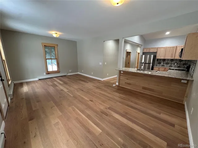 a view of kitchen and empty room with wooden floor