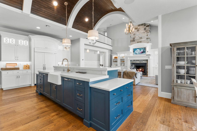 2917 Old Farm Road Washington, UT 84780 - Photo 17 of 105 Kitchen featuring two tone color scheme, light wood-style flooring, an island with sink, a stone fireplace, and light stone countertops