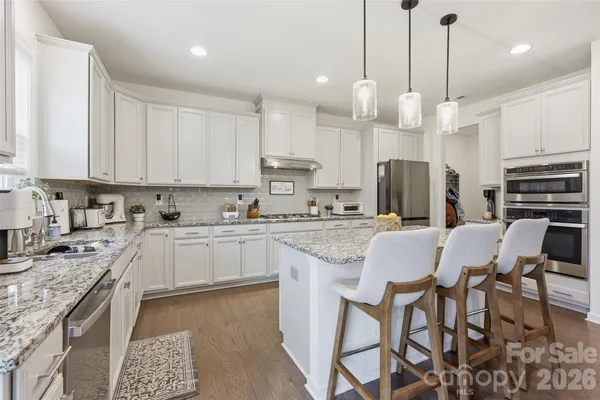 a kitchen with stainless steel appliances granite countertop a stove top oven a refrigerator a sink and white cabinets